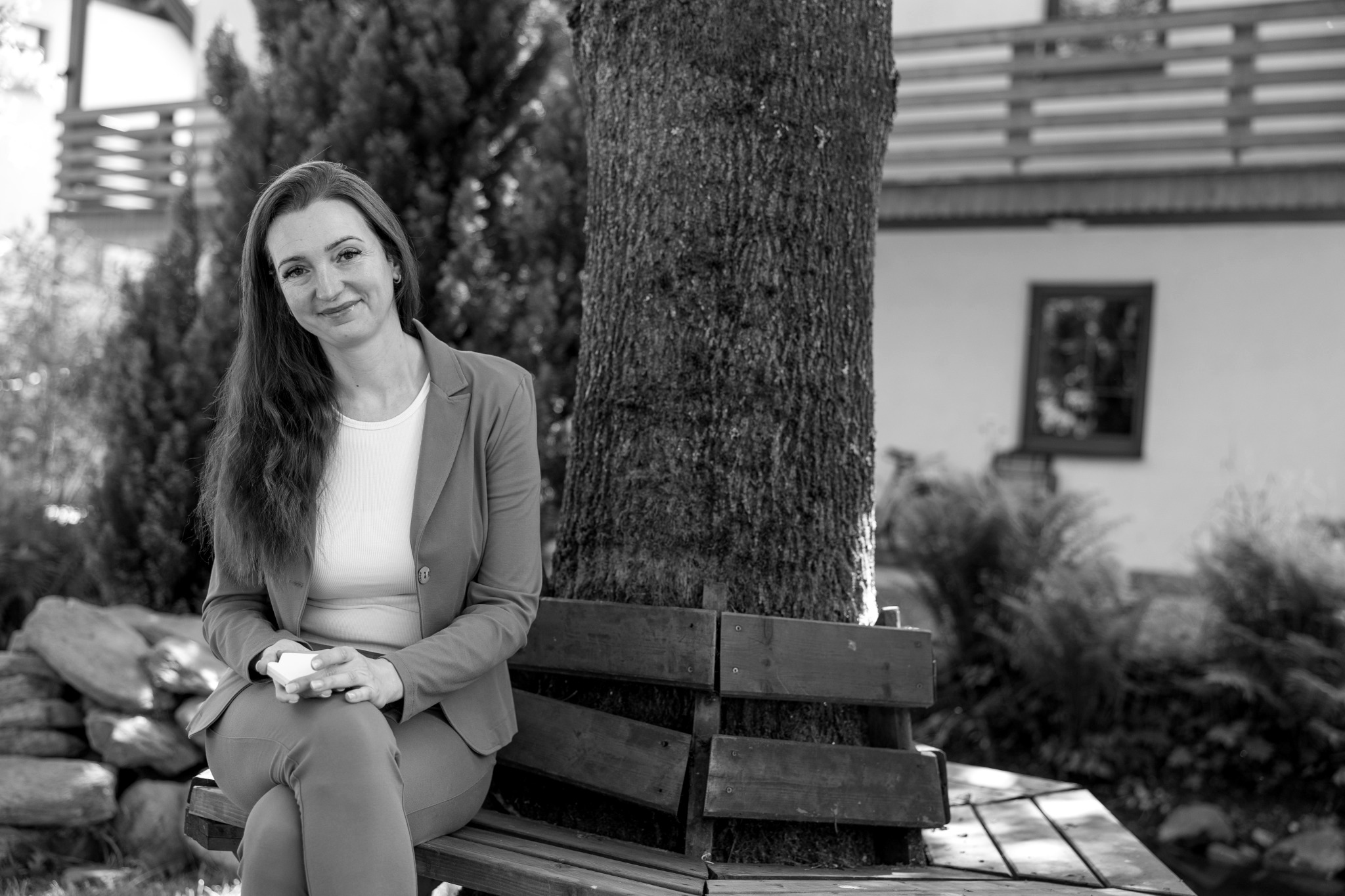 Lucka Kačerová sedí na lavičce pod stromem na zahradě.